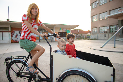 Mid adult woman riding her two happy sons in the cargo bike.