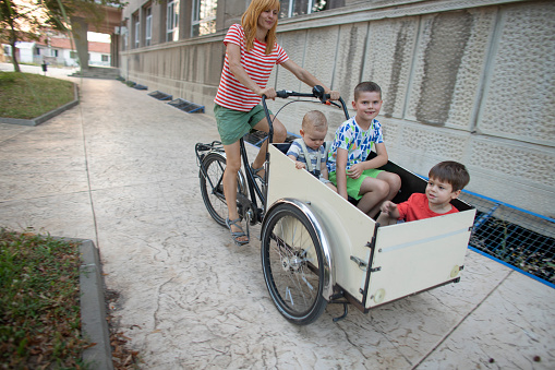 Mid adult woman riding her three happy sons in the cargo bike.