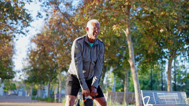 Senior black man strength training with kettlebell in the morning light at a park