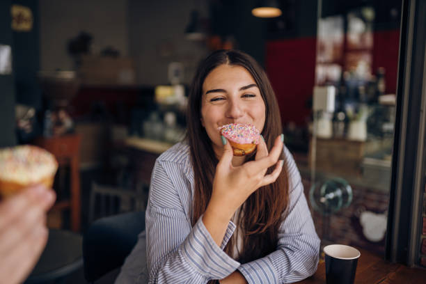 Coffee and doughnuts, my favorite treat Young woman having a coffee break and eating a doughnut coffee cup and donut stock pictures, royalty-free photos & images