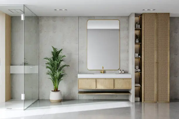 A contemporary bathroom design featuring a glass shower enclosure, a minimalist vanity with a gold-accented mirror, and a tall woven storage unit. 
The neutral color palette is complemented by a touch of greenery from the potted plant.