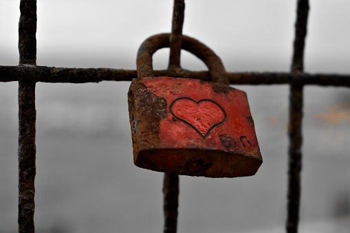 Red heart love shaped padlocs are hanging on the metallic bars fence covered with snow