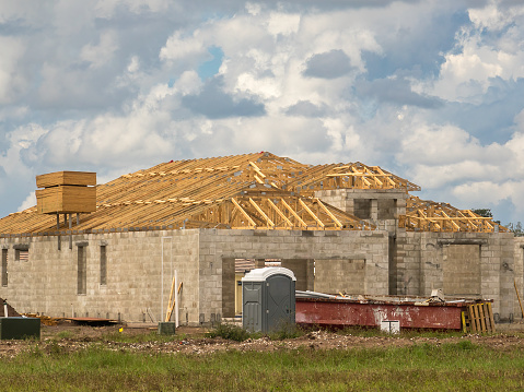 Single-family house under construction, with concrete shell and wooden roof trusses, in a suburban development on a cloudy day in southwest Florida