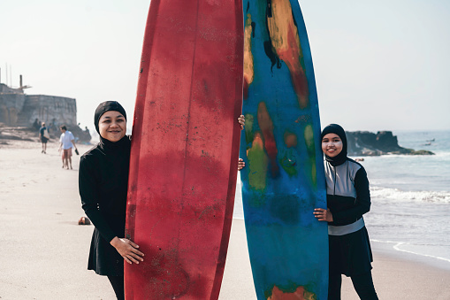 two muslim woman  preparing to go surfing at dawn