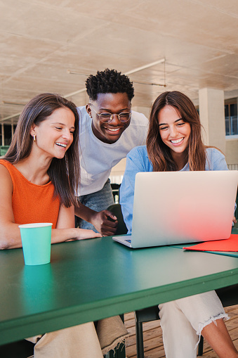 Vertical portrait of a group of multiracial happy teenage students using laptop, working on university homework project in college library. Meeting of young people looking information on computer. High quality photo