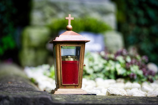 metal grave lantern with cross in front of old tombstone in blurred background