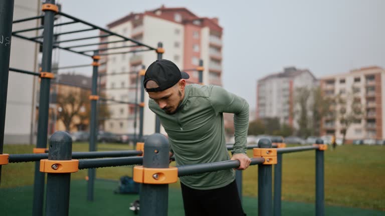 Young Man in Sportswear Doing Pull-Ups Exercise on Horizontal Bars in Park