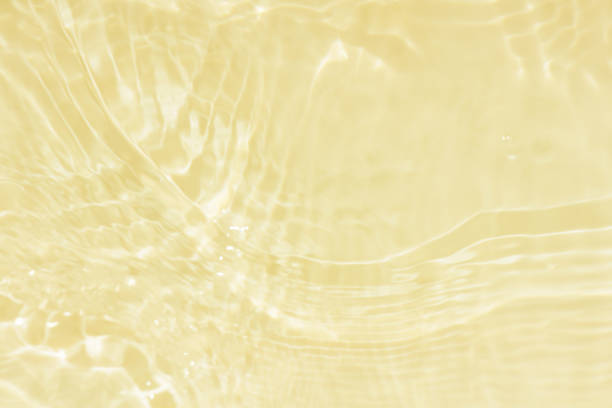 Defocus blurred transparent gold colored clear calm water surface texture with splashes reflection. Trendy abstract nature background. Water waves in sunlight with copy space. Orange watercolor shine.