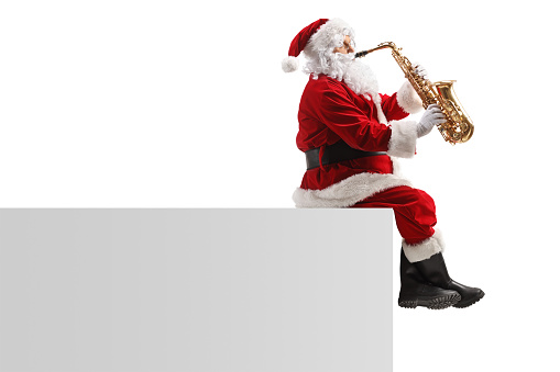 Profile shot of Santa claus sitting on a wall and playing a saxophone isolated on white background