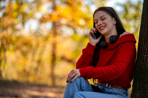 A beautiful young woman uses a phone to surf the web in an autumn park.