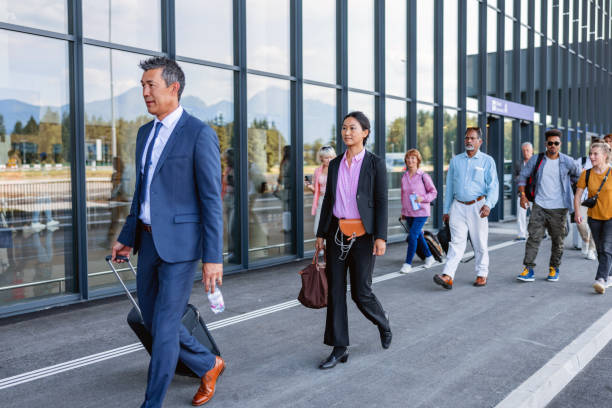 Busy Airport Arrival: Diverse Travelers with Luggage Outside Terminal A diverse group of travelers, including businesspeople and tourists walking outside the terminal with their luggage. walking into glass door stock pictures, royalty-free photos & images