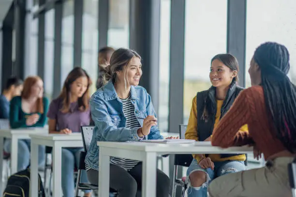 University students are seen scattered at various desks in an open study area, as they work away on assignments between classes.  Some students are working together while others are seen working independently.