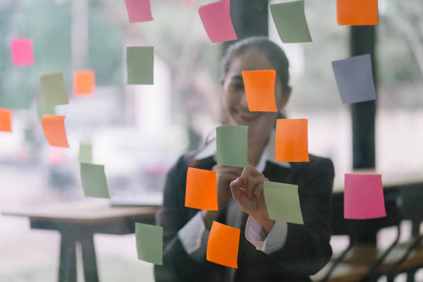 istock Businesswoman writing notes about teamwork decisions for project plan, tasks, or ideas on sticky notes in startup workplace. 1758844540