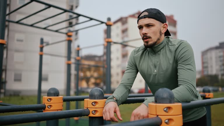 SLO MO Tired Young Athlete in Sportswear Leaning on Horizontal Bars Taking Rest After Intense Workout in Park