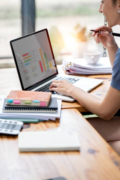istock Business woman sitting working on laptop computer with financial graphs and statistics on monitor. 1758872516