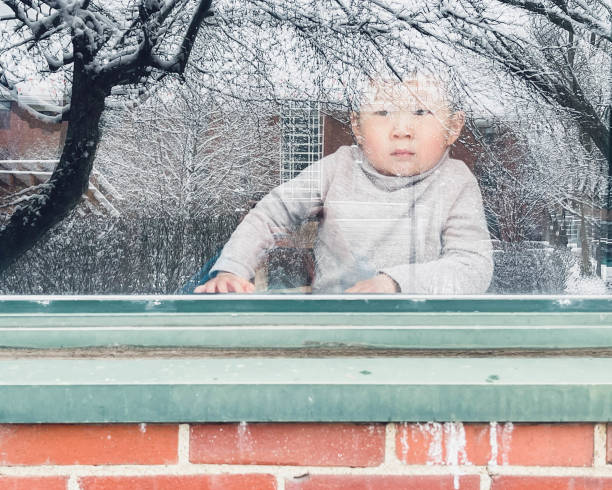 Boys looking out the window on a snowy day. The backyard glows with light