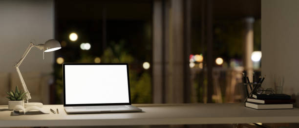 istock A white-screen laptop mockup, a table lamp, and accessories on a table in a modern room at night. 1758905137