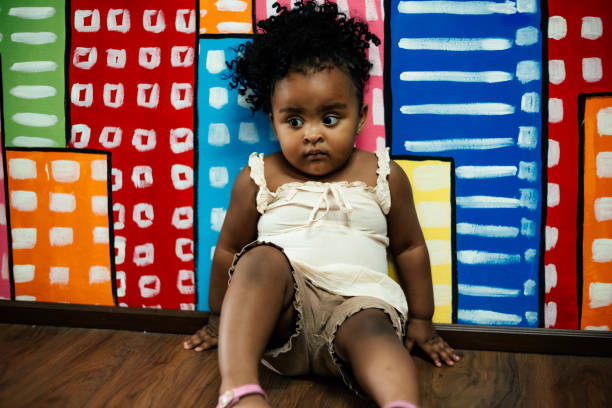 Cute little baby African girl sitting in home