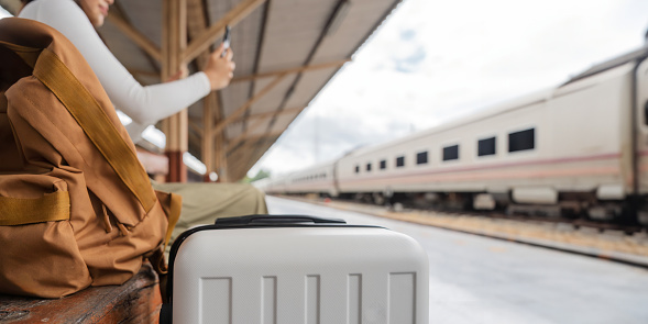 Asian female traveler using her smart phone mobile while waiting for a train at a station.