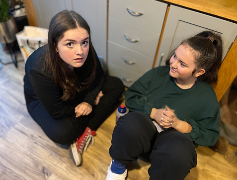 Two teenage female cousins in conversation sitting on wood floor