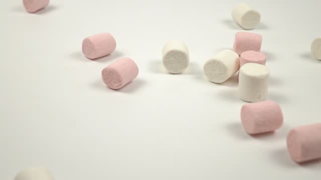 Pink and white marshmallows fall on a white table, slow motion