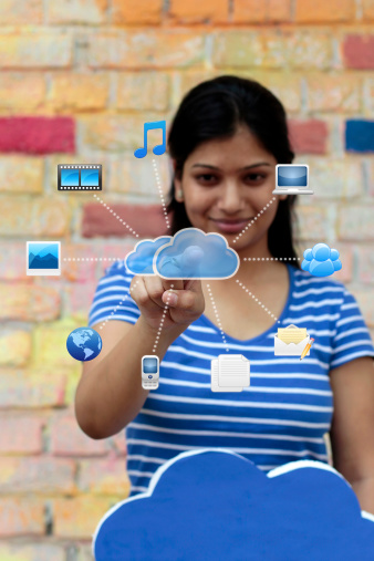 Cloud computing technology with a female touching the figure of a cloud connecting to different symbols showing multimedia, documents, internet, computer, etc. (Note: The image has a shallow depth of field with focus at the hand)