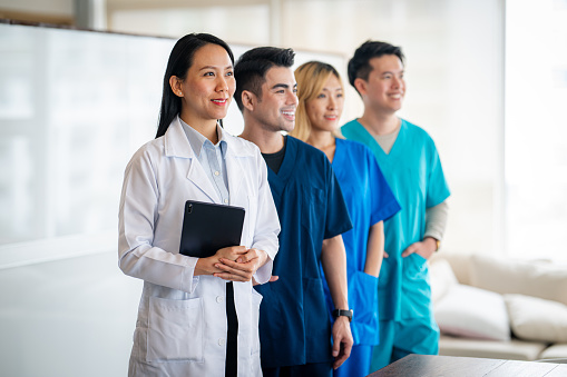 A smiling group of Asian doctors and nurses in the doctor's office portrait.