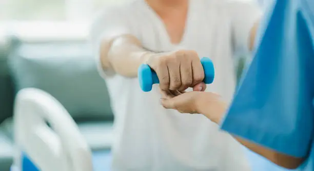 Physical therapist giving exercise by maintaining dumbbells on the arms and shoulders of a male patient. Physical therapy concept