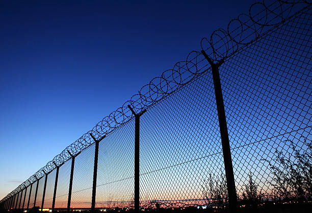 Photograph of a fence for a restricted area Barb wire fence at dusk - protection of Warsaw airport area (Poland). barbed wire photos stock pictures, royalty-free photos & images