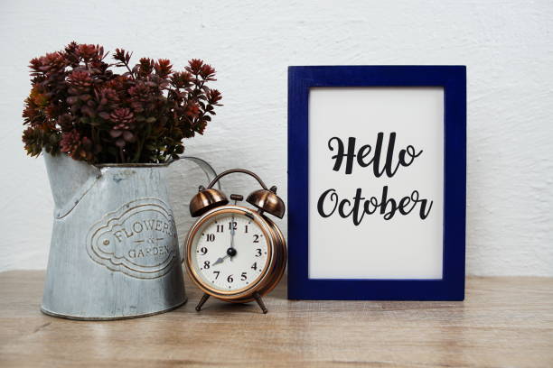 istock Hello October typography text with alarm clock and artificial plant decoration on wooden table and white wall background 1759174187