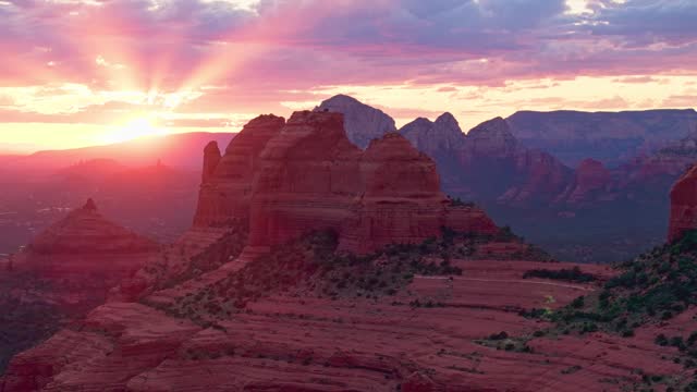 Incredible sun rays pierce clouds spreading pink glow above Merry Go Round red rock Sedona Arizona, drone landscape