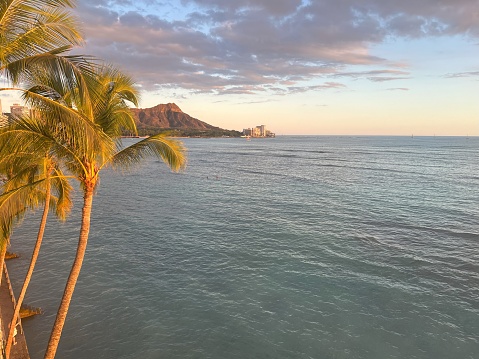 Beautiful sunset reflection in the sky with diamond head and pacific ocean with swimmer in the water at a distance. Clouds in Hawaii sky.