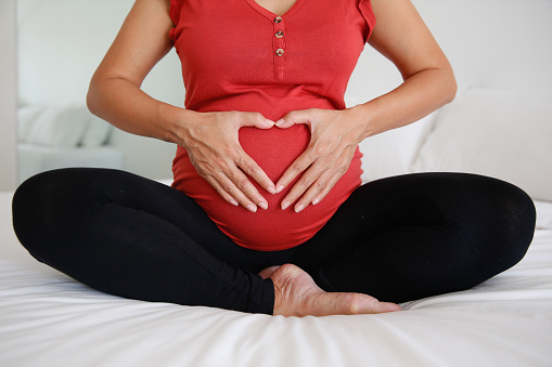 Beautiful pregnant woman hugging her belly in white background. Expectant mother waiting for baby birth during pregnancy. Concept of maternal health, visiting doctor and gynecological checkup.