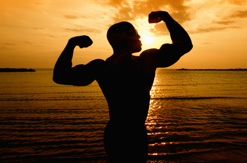 Silhouette of one bodybuilder posing at the sunrise on the beach