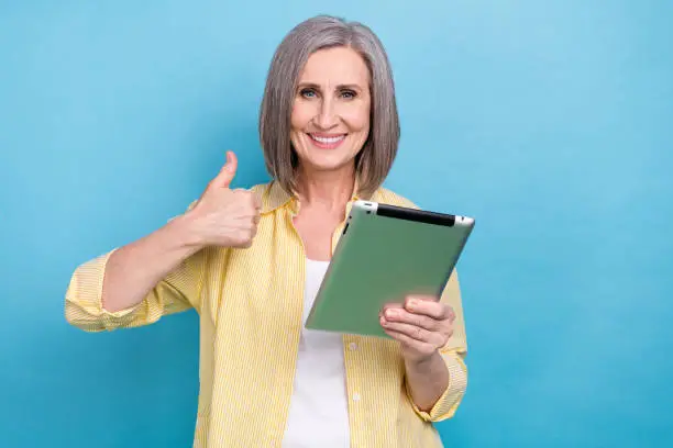 Photo of sweet confident woman dressed yellow shirt thumb up working apple samsung iphone device isolated blue color background.