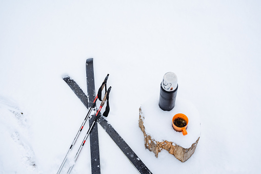 false poles and skis lie on the snow, next to a stump with a thermos and a mug of tea. Winter still life in the snow. Skiing in the woods, fresh air. High quality photo
