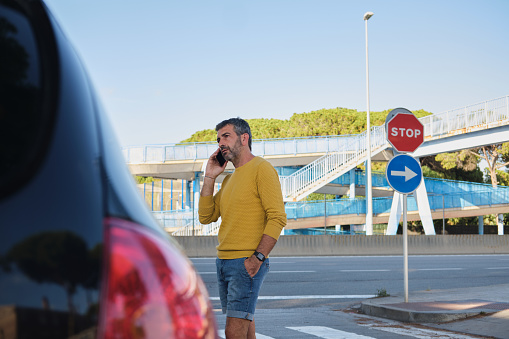 front view portrait of a European generation x man near a road solving some car issues talking by the phone before drive to going to work