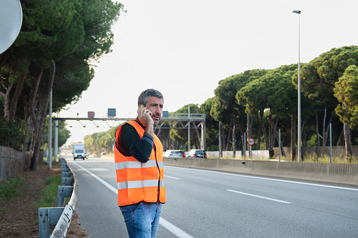 side view portrait of a European generation x man talking by the phone and waiting to the car tow truck near a road