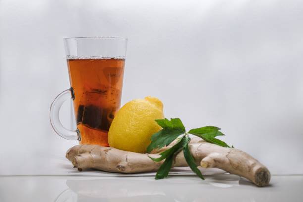 istock Clear glass mug filled with steaming hot tea with a lemon and ginger atop a white table 1759290317