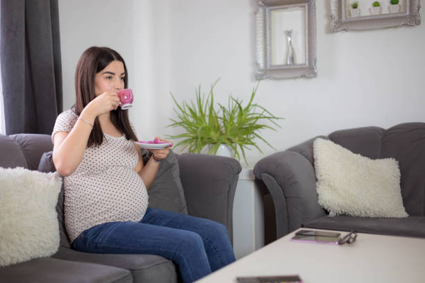 istock Pregnant woman drinking tea, while watching TV 1759312413