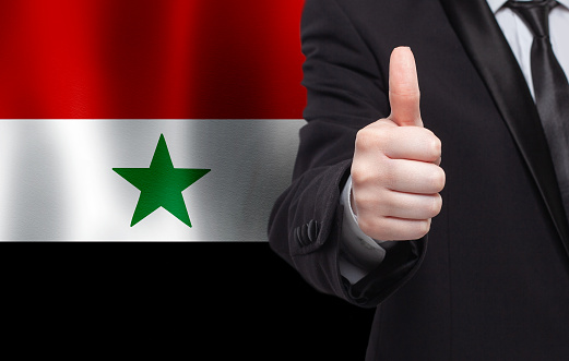 Syrian concept. Businessman showing thumb up on the background of flag of Syria