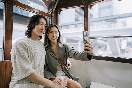 Tourist Asian Chinese couple selfie in retro double decker bus in Hong Kong trip with smart phone