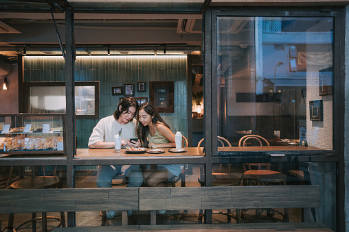 Happy young Asian couple dating in cafe, drinking chatting. Enjoying moment together