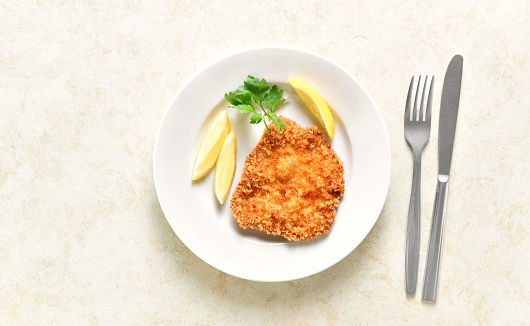 Homemade breaded chicken schnitzel on plate over light stone background. Top view, flat lay