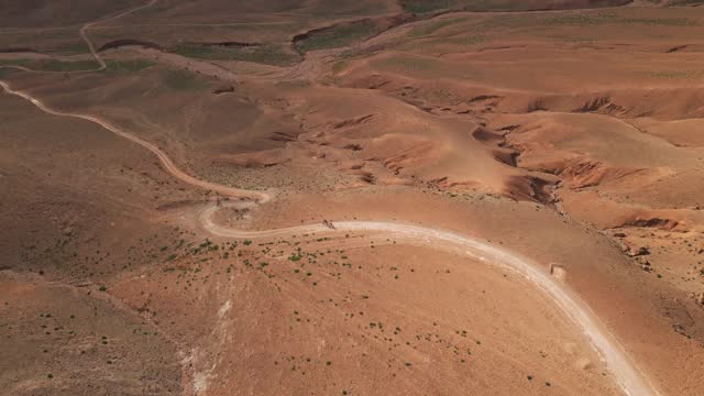 Mtb riders ride a long winding dirt road in the middle of the mountains in Morocco.