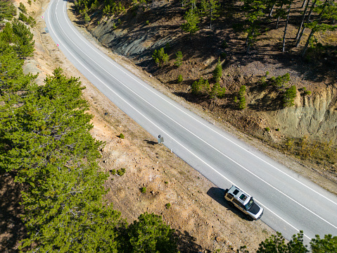 Curvy forest road. Asphalt road. Off road vehicle standing on the roadside.Drone shot from the air, bird's eye view.