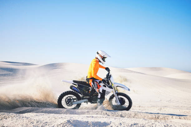 istock Extreme sport, motorcycle and athlete with sand by wheels with pride, skill and adrenaline rush.  Biker, sunshine and dust with blue sky in fun, fitness and achievement in speed, race and lens flare 1759411607