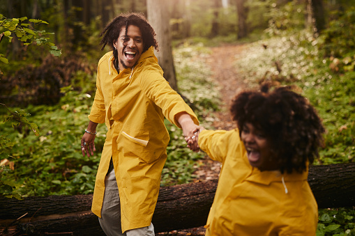 Happy African American man having fun while holding hands with his girlfriend during autumn day in the woods.