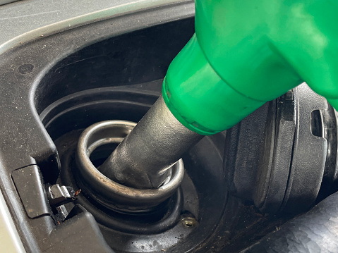 Stock photo showing close-up view of car fuel tank being filled by an  unleaded petrol pump nozzle, whilst on forecourt at fuel filling station.