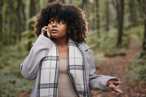 Displeased African American woman arguing with someone over mobile phone during autumn day in nature.